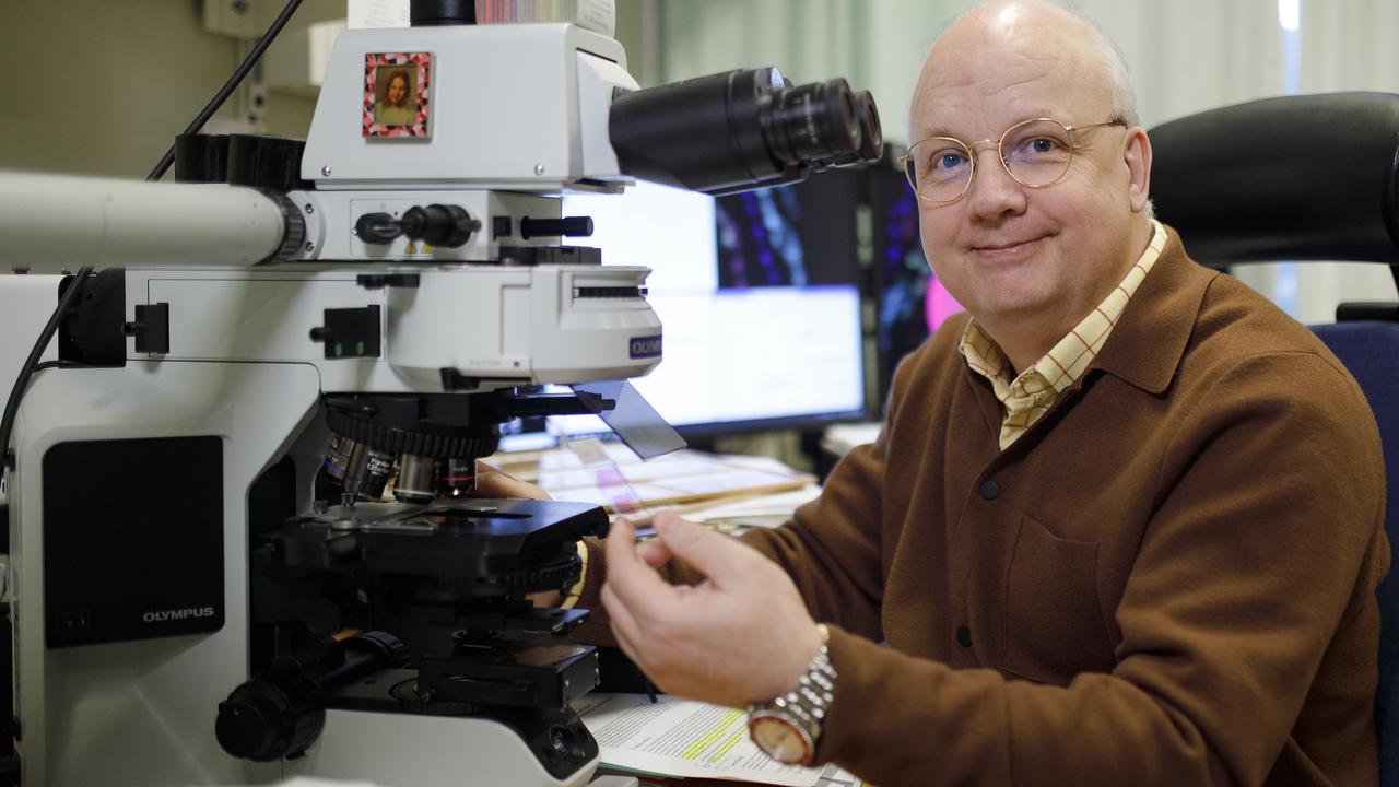 Thomas Brännström sitter vid sitt mikroskop och ler mot kameran med ett glas med vävnadssnitt i handen.