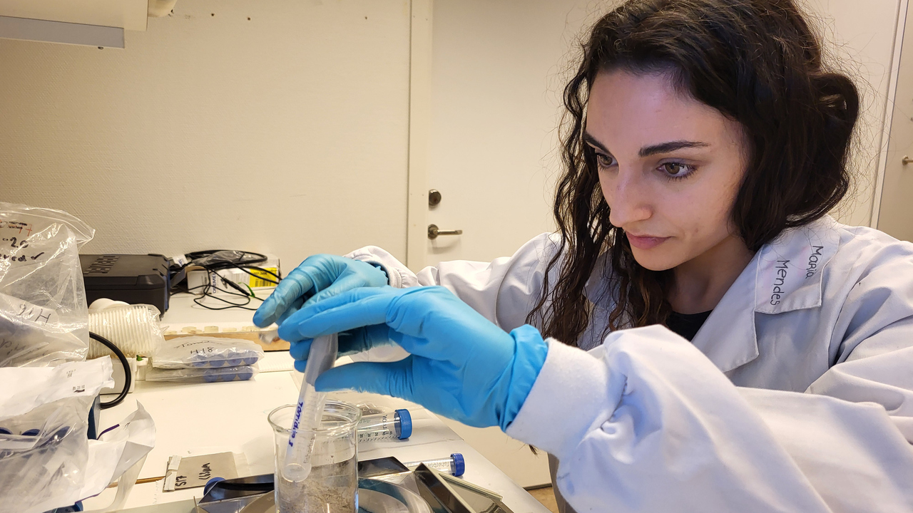 En ung kvinna med vit labrock och blå plasthandskar på sig väger prover på en våg.