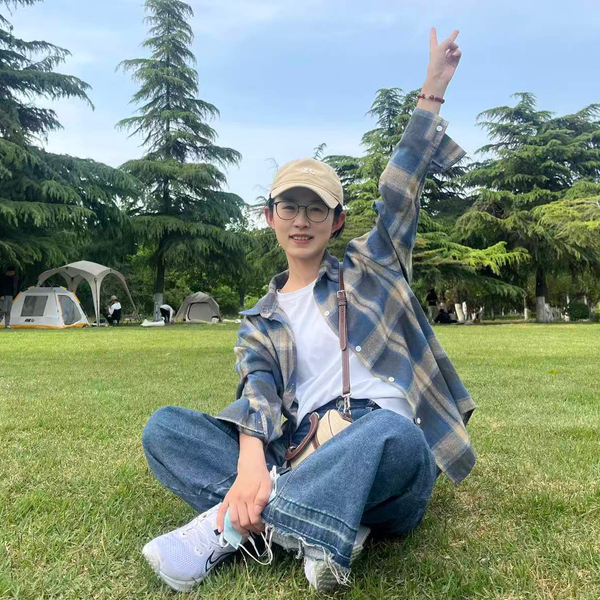 Xue-Chan Tian sitter med korslagda ben på en madrass och sträcker upp sin högra hand i luften och visar ett segertecken