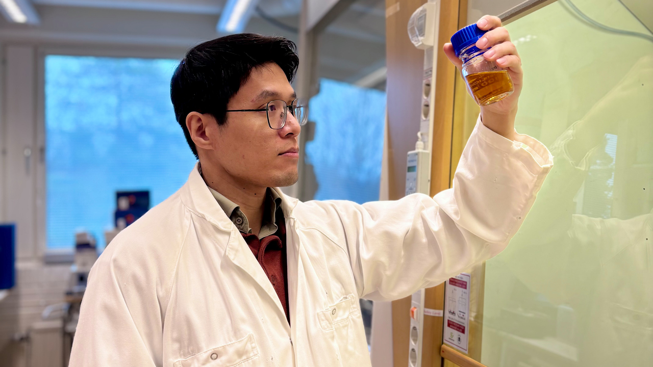 Bild på doktoranden Van Minh Dinh i vit labbrock stående intill ett dragskåp, håller ett preparat i vänstra handen.