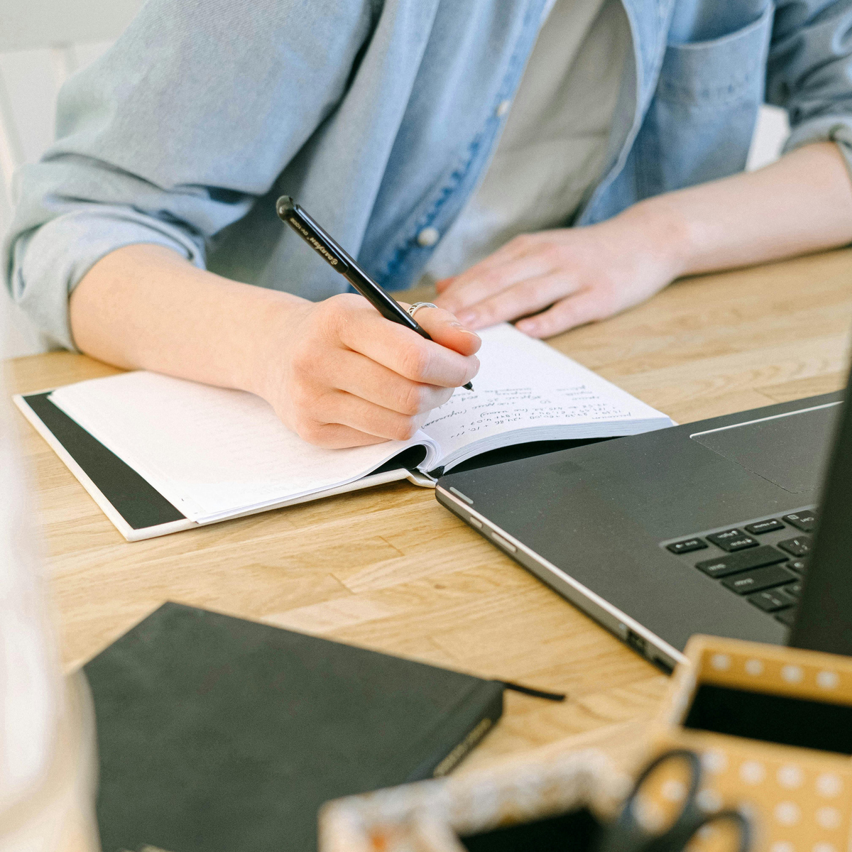 Hand som antecknar framför en laptop.