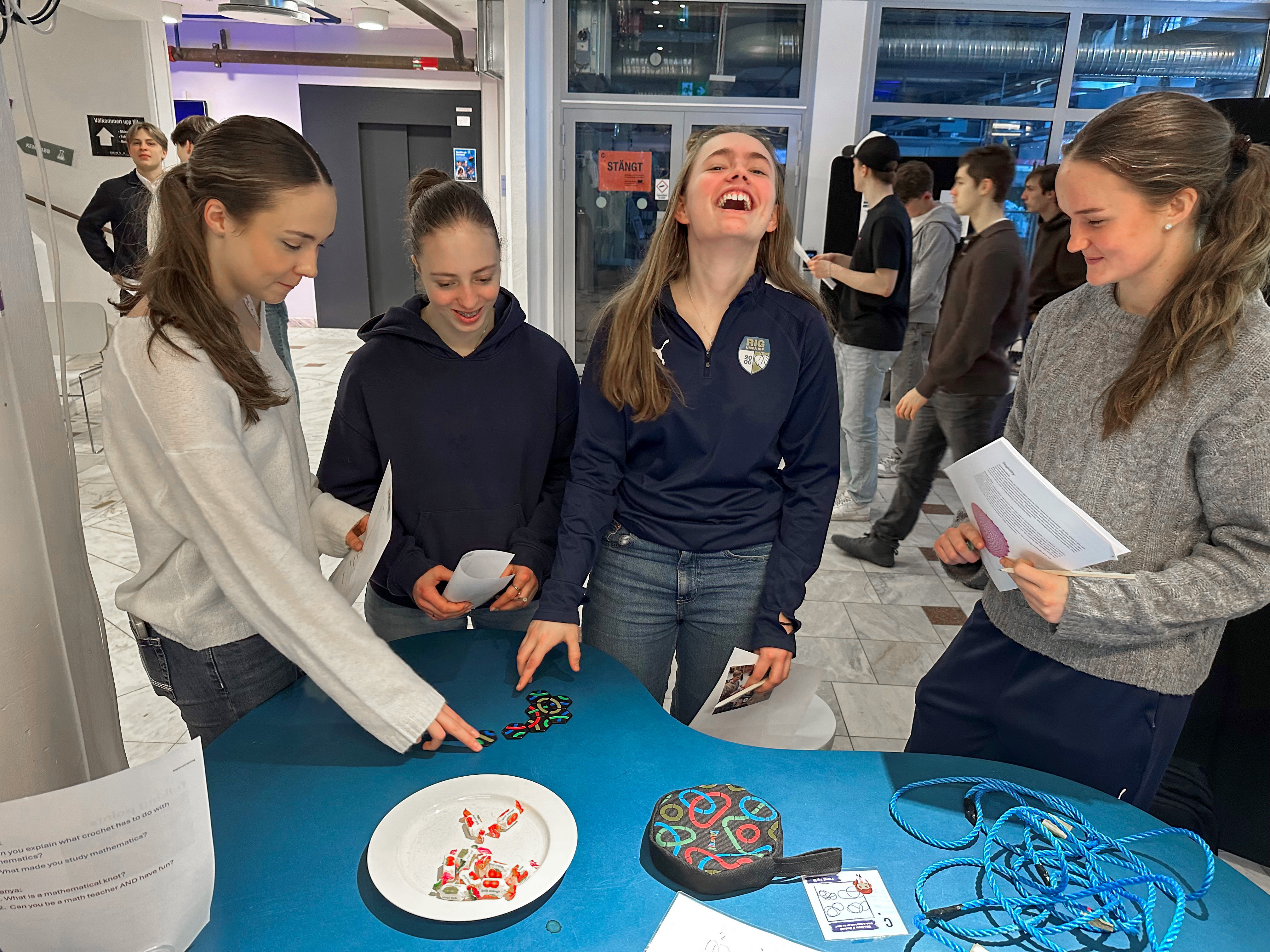 Fyra unga kvinnor deltar i semifinalen av Unga forskare, som arrangerades i Umeå den 28 februari. De står runt ett blått bord och interagerar med färgglada knutar, rep och informationsblad.