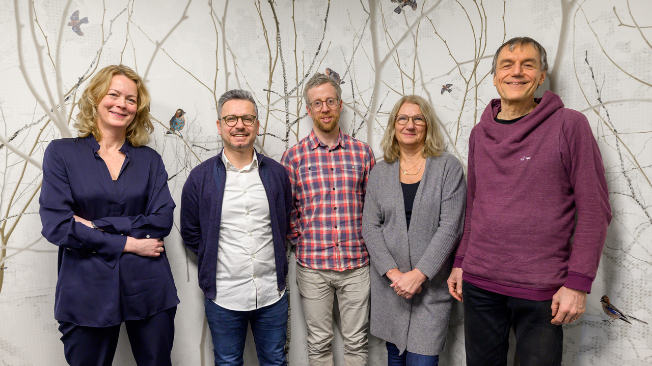 Fem personer står framför en bakgrundsbild av en skog med fåglar