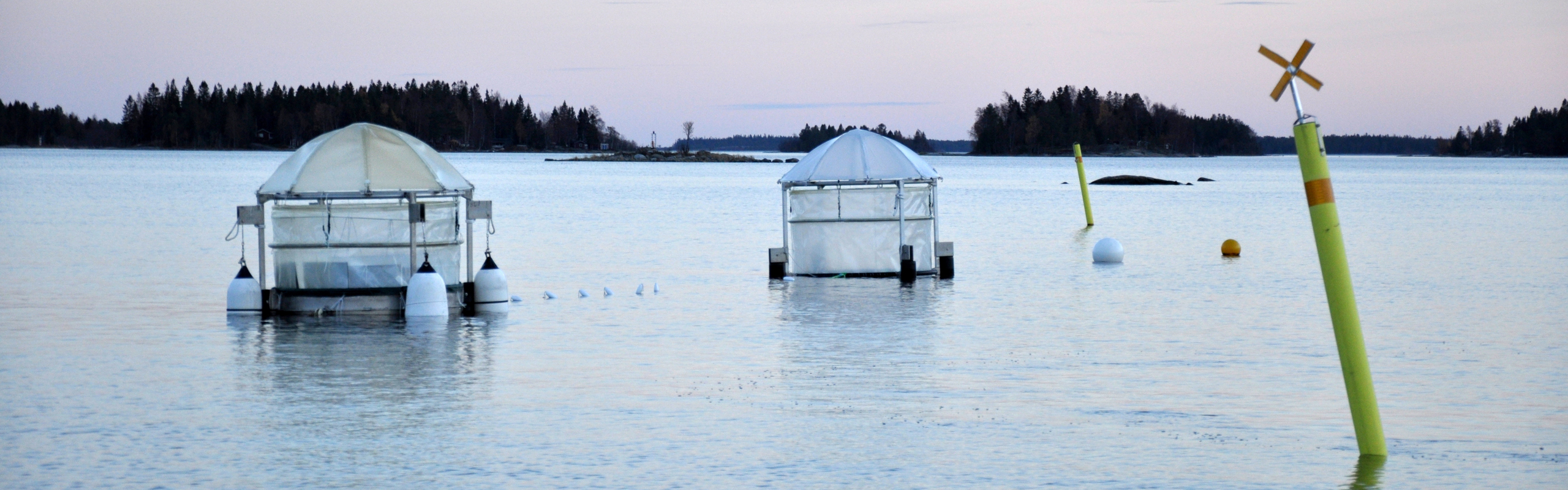 Två mesokosmer förankrade i havet med ett sjömärke i förgrunden