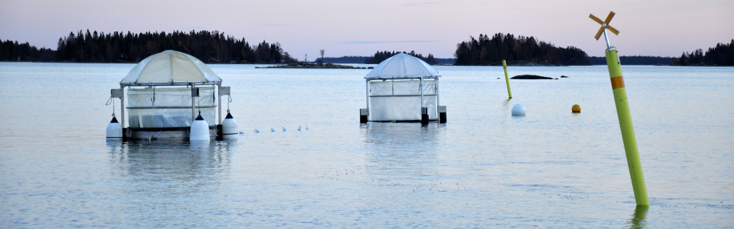 Två mesokosmer förankrade i havet med ett sjömärke i förgrunden