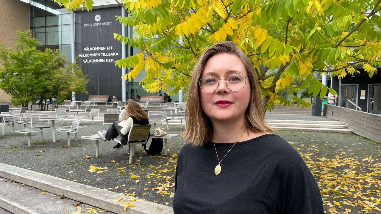 En kvinna med glasögon står framför en byggnad.