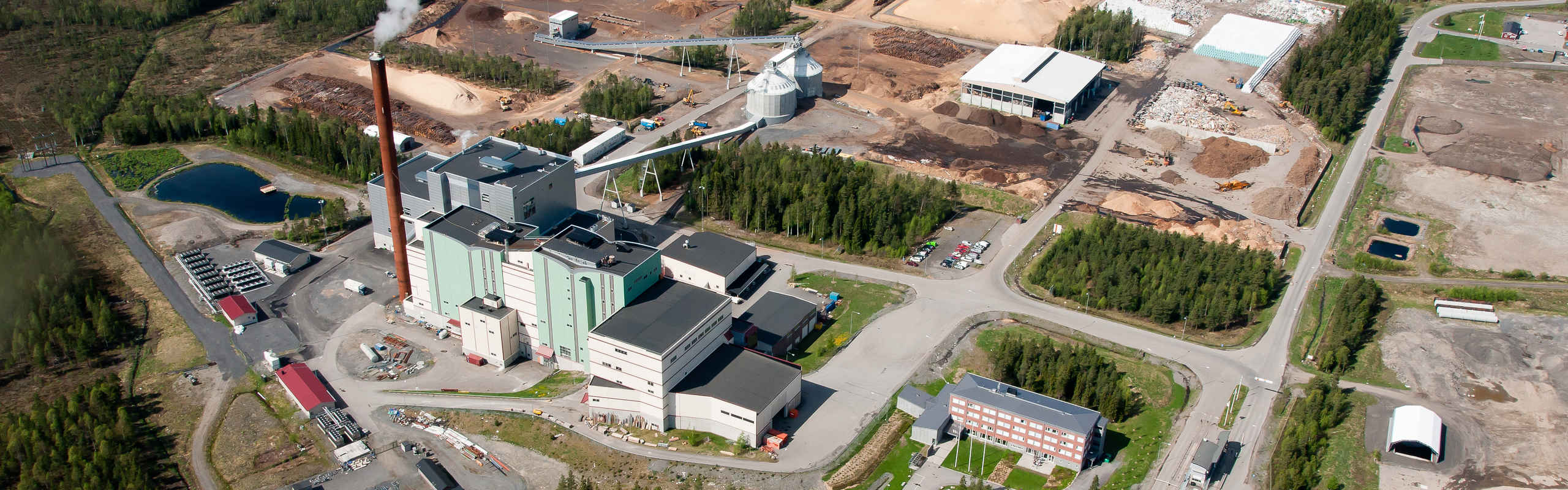 Flygbild över kraftvärmeverk omgivet av skog.