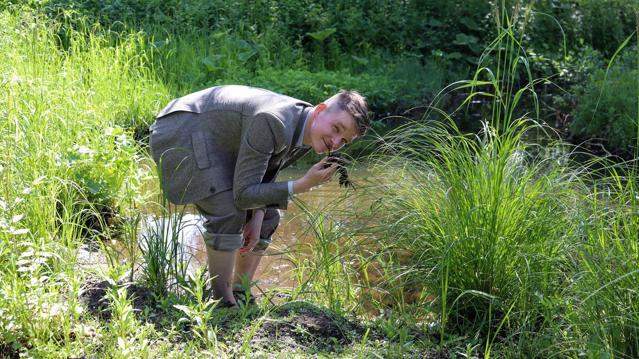 En man står i en bäck och luktar på dy.