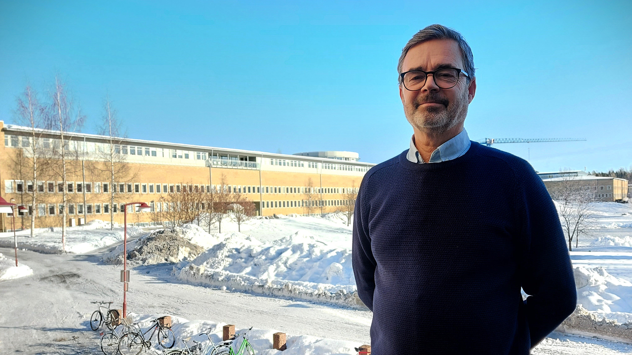Man står utomhus med samhällsvetarhuset i bakgrunden. Solen lyser och det är vinter.