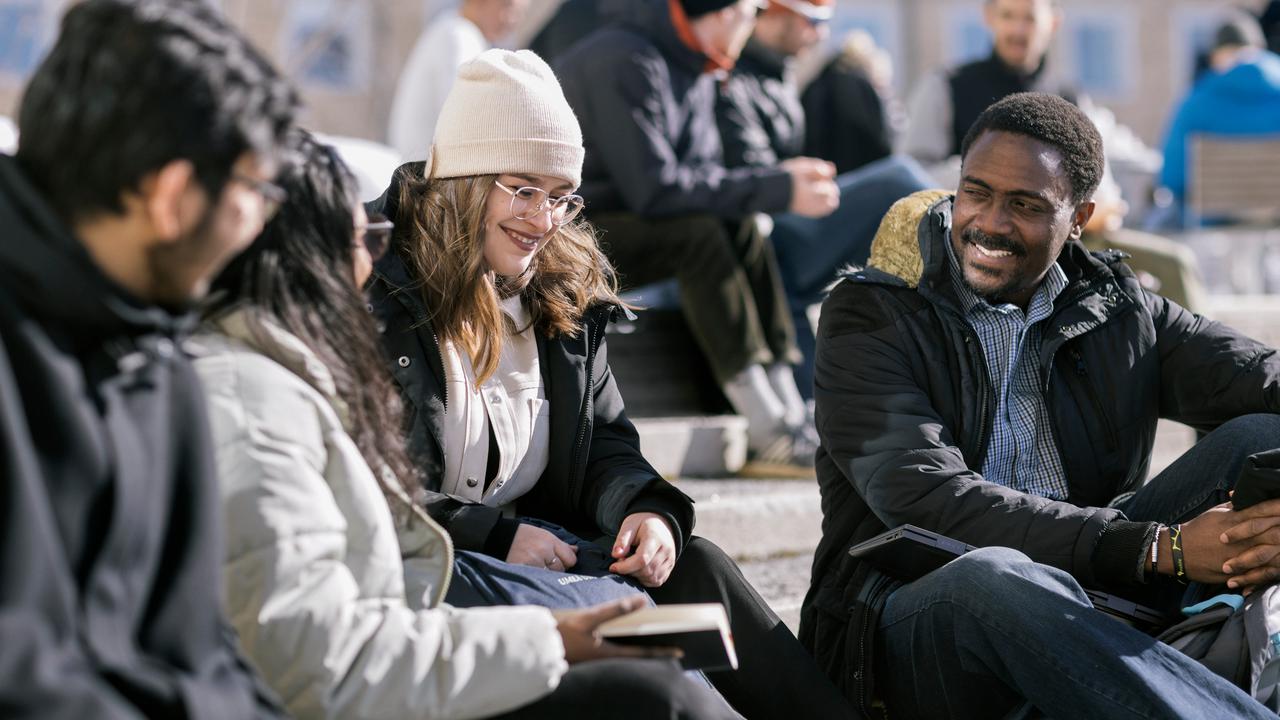 Several students in winter attire in the warming spring sun on Campus Umeå.