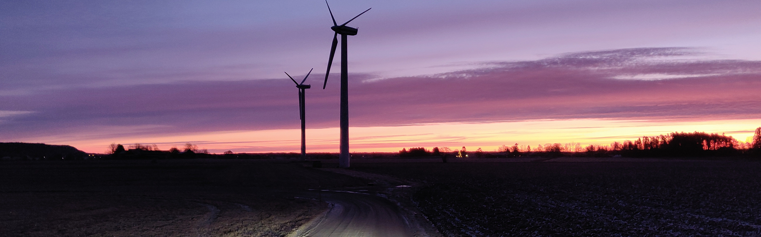 Vindkraftverk i tidig gryning och en bilväg.