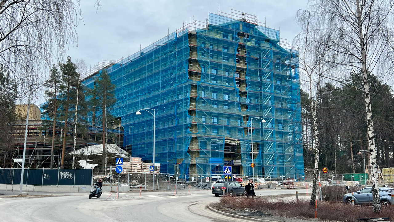 Byggnaden håller på att uppföras, och har byggställningar och blå nät på fasaden.