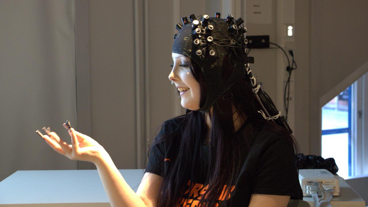 En kvinna i svart skjorta sitter med en hetta som visar hjärnktivitet.