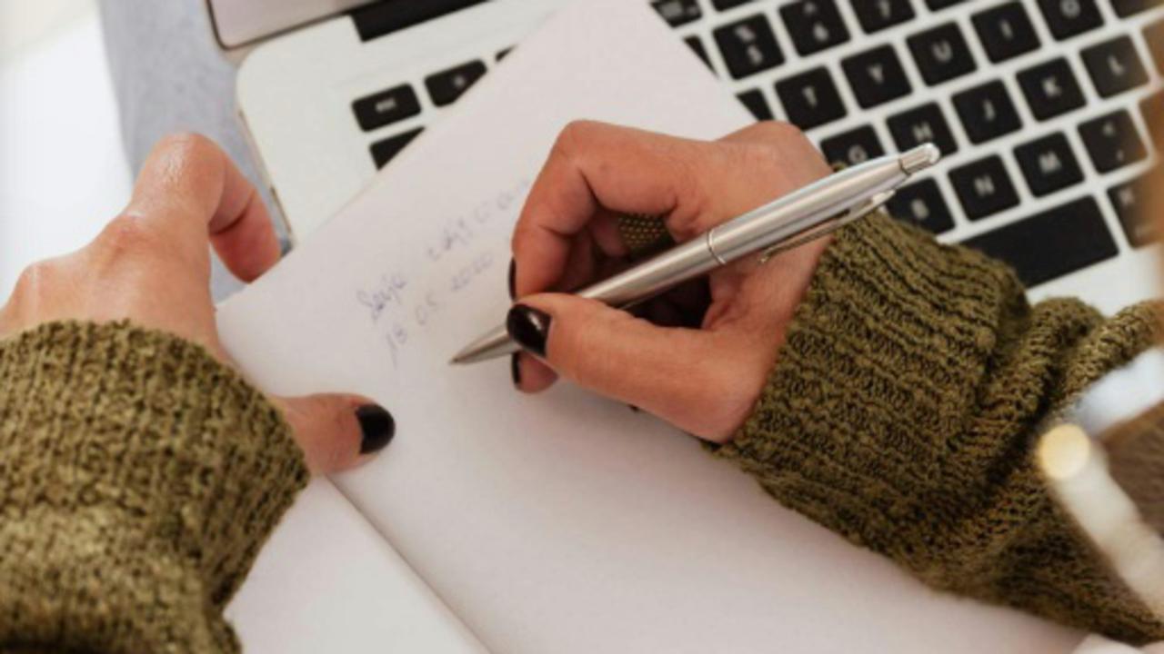 Hands writing on a piece of paper at a computer