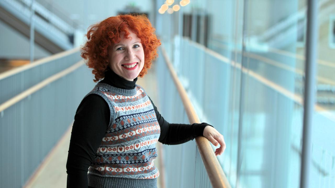 En kvinna med rött hår står på en balkong.