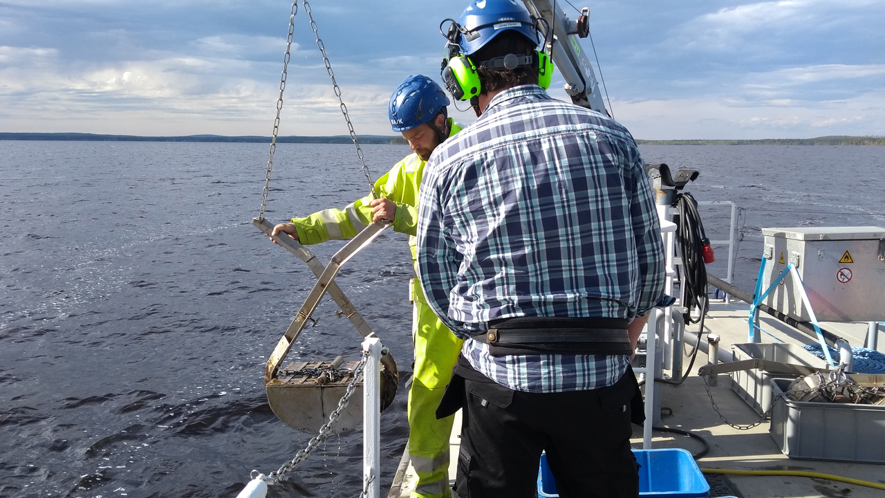 Två personer står vid en fartygsreling och hanterar en bottenhuggare
