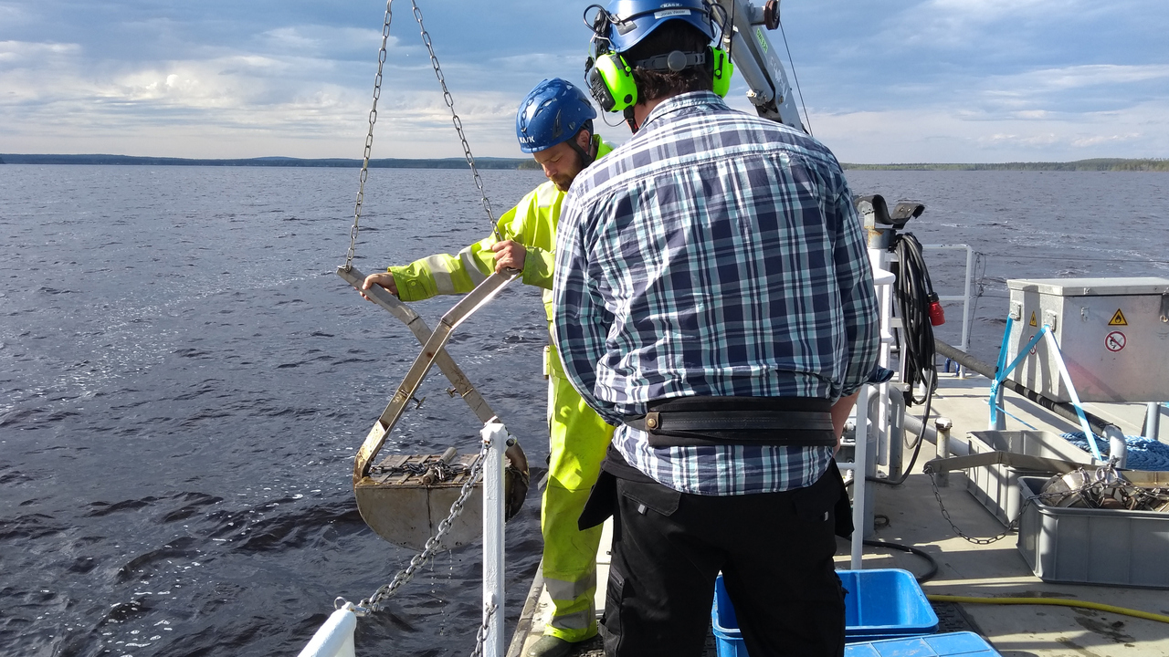 Två personer står vid en fartygsreling och hanterar en bottenhuggare