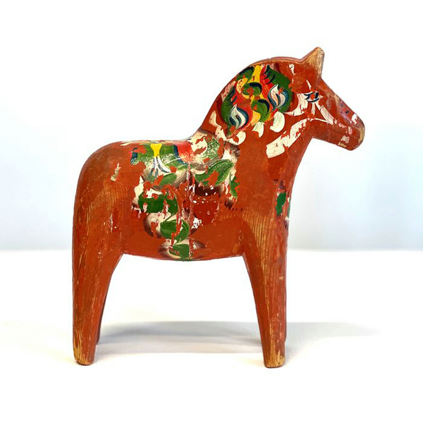 En gammal, röd dalahäst med målat mönster i grönt, vitt och gult.