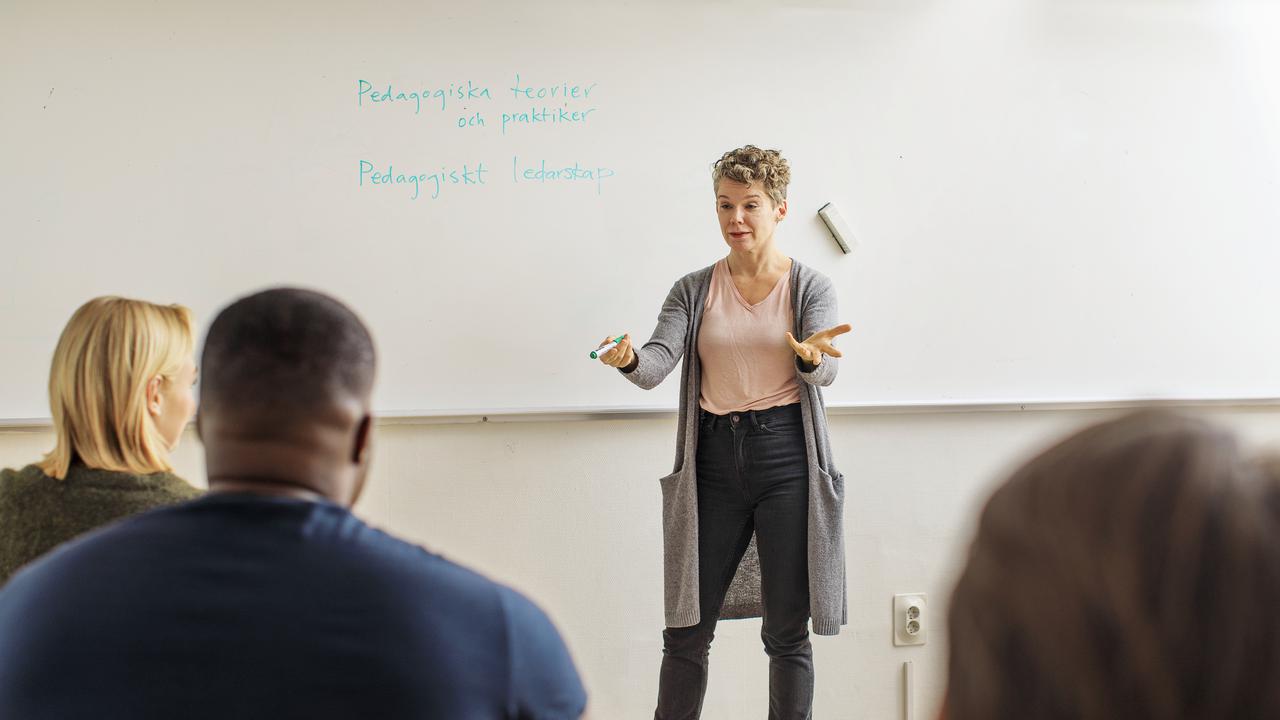 Lärare undervisar vuxna i klassrum.