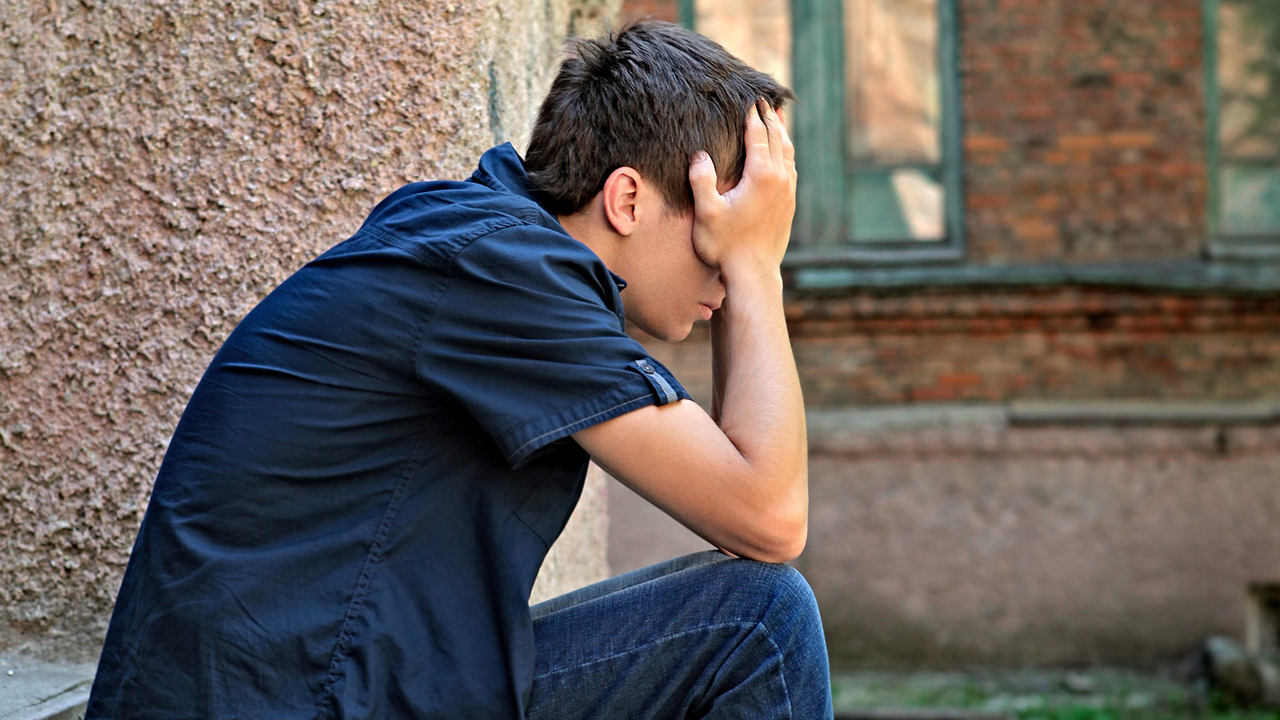 Ledsen eller deprimerad man sitter utomhus med huvudet i händerna.