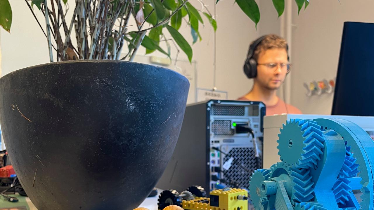 En person som står och jobbar vid sin dator med prylar i framgrunden