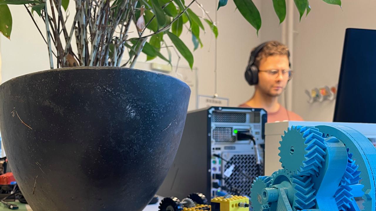 En person som står och jobbar vid sin dator med prylar i framgrunden