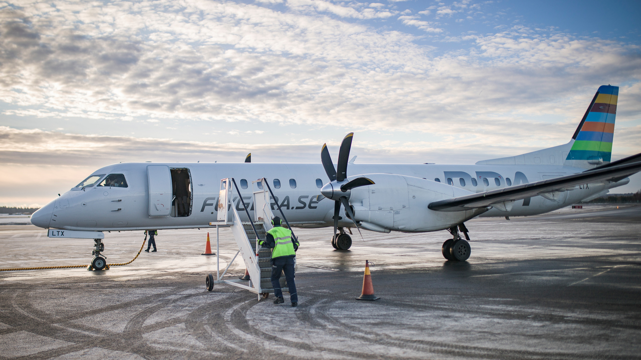 Ett flygplan som står på landningsplattan på Umeå flygplats. En flygplatsanställd håller på att ansluta trappan för att passagerare ska kunna gå ur planet.