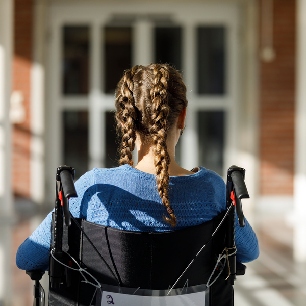 Flicka med flätor sitter i rullstol framför byggnad.