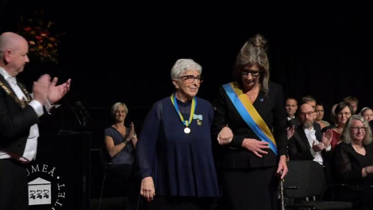 Två kvinnor i armkrok går fram på en scen.