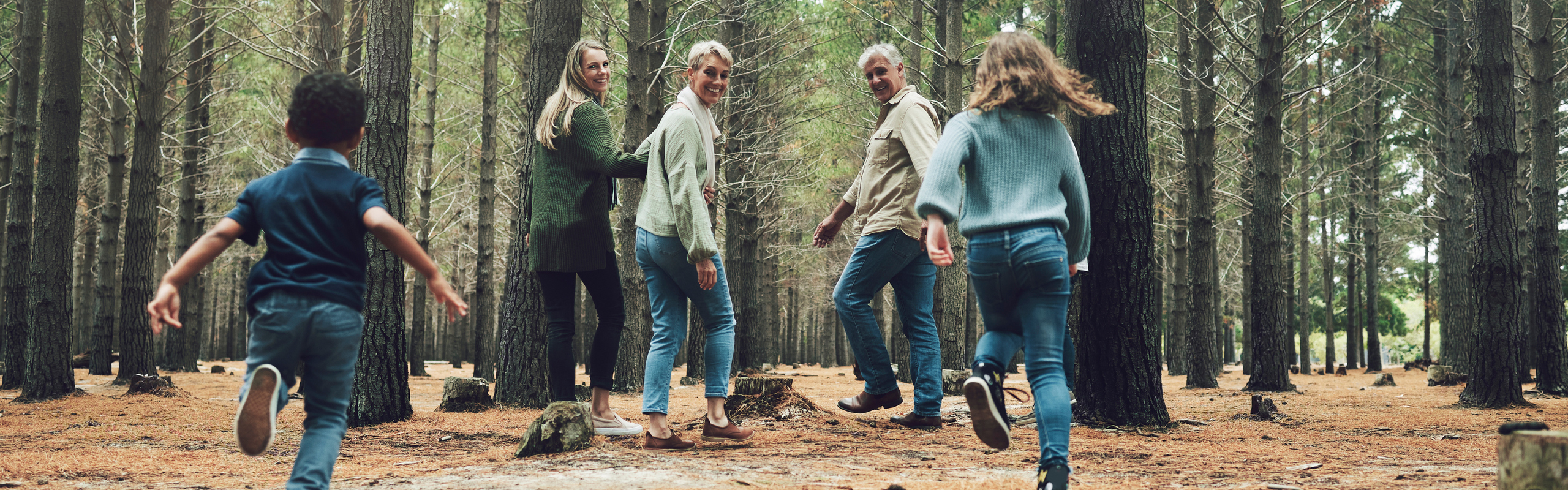 Familj med barn ute på promenad i barrskog.