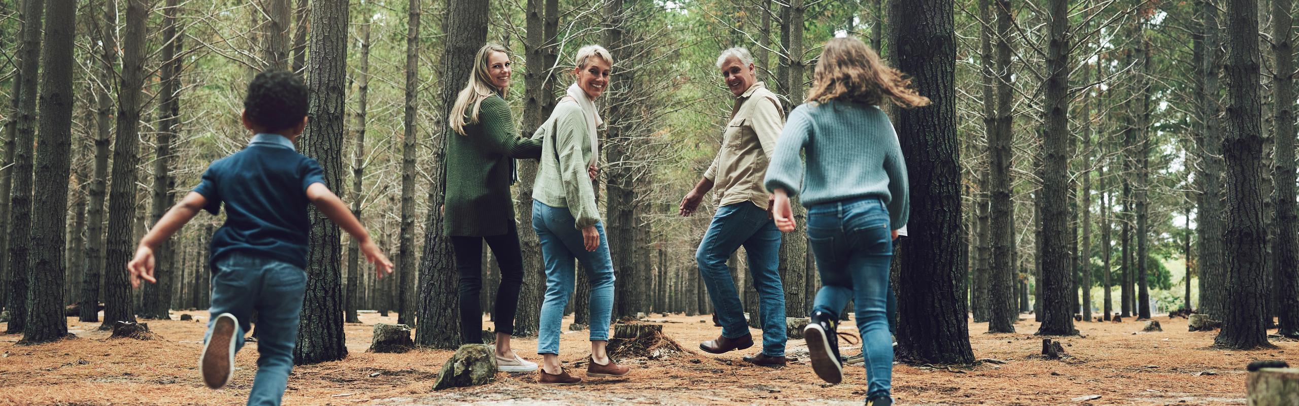 Familj med barn ute på promenad i barrskog.