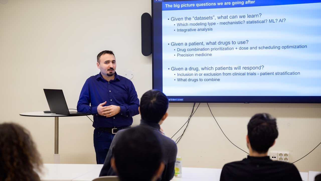 Cemal Erdem stands in front of a screen with a slide displayed describing his current research
