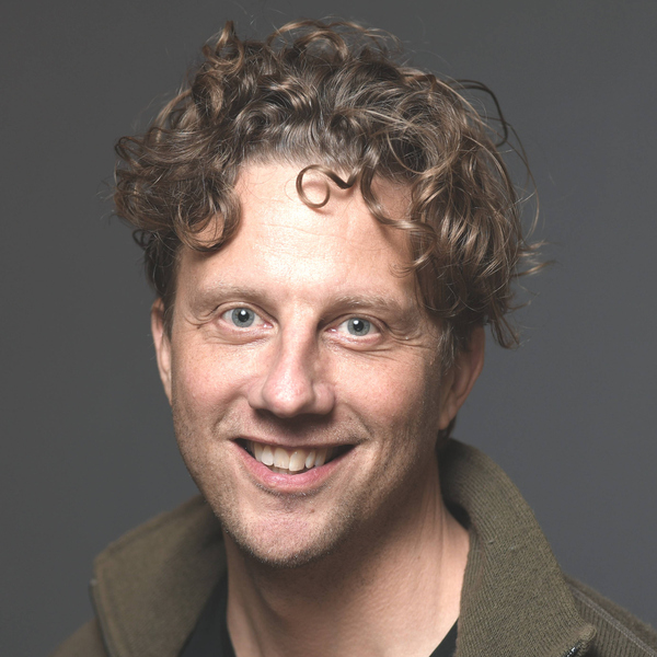 Man med lockigt hår ler och tittar in i kameran.