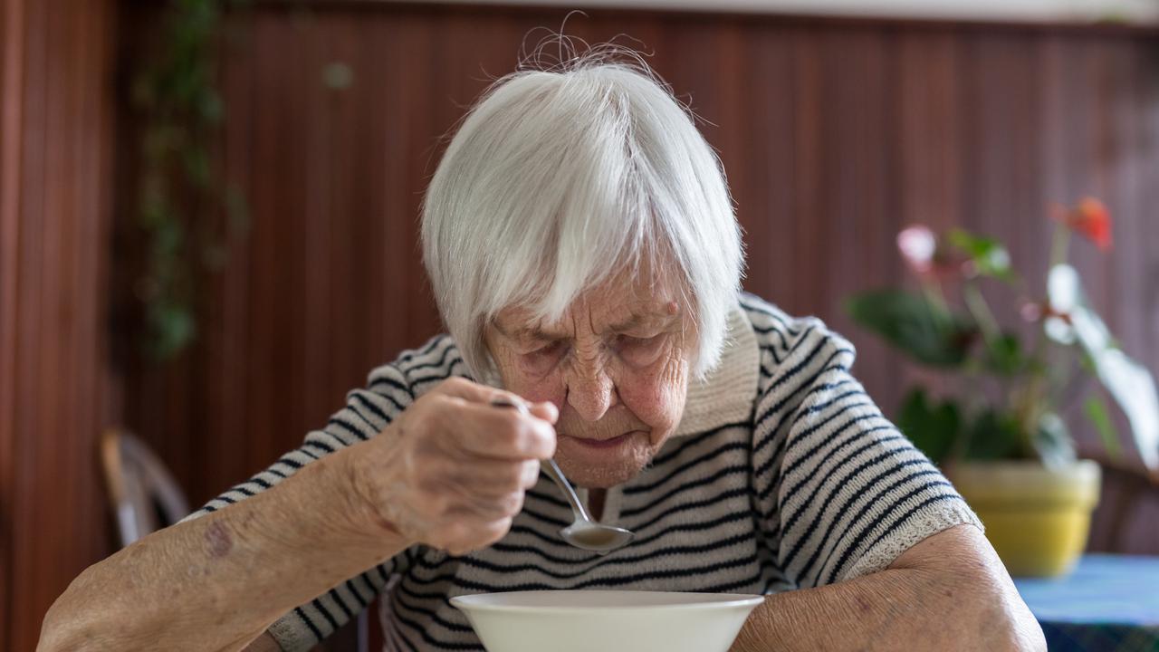 Äldre kvinna sitter på en veranda och äter fil ur en tallrik.