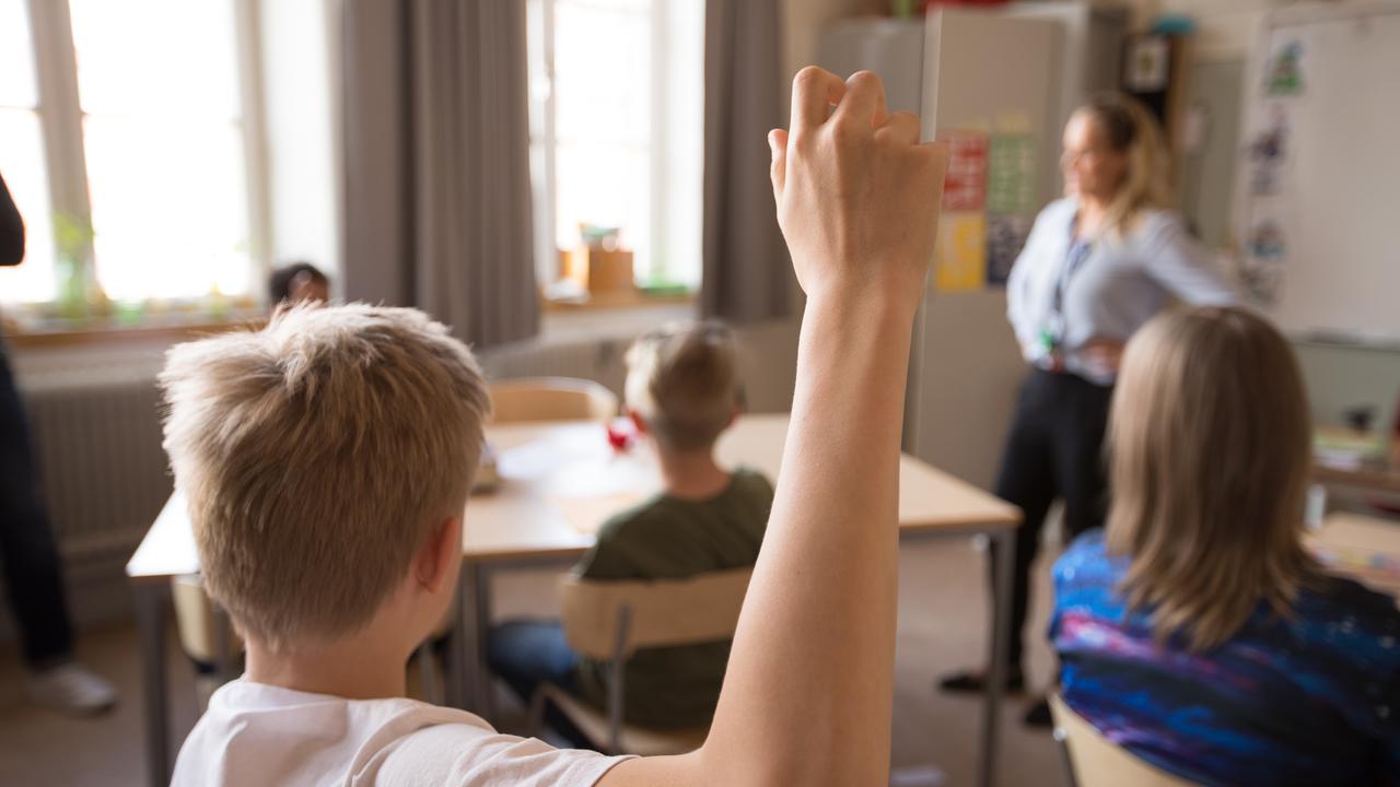 Mellanstadiebarn i klassrum. Pojke räcker upp handen.