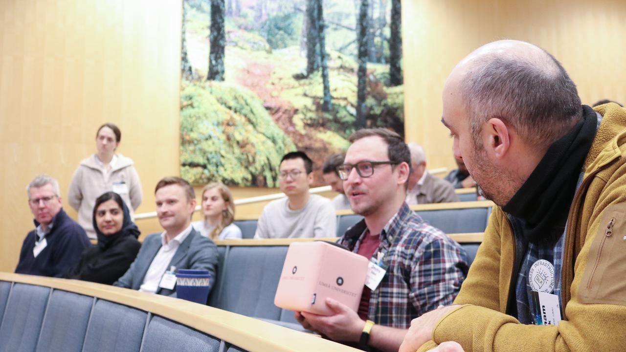 A group of people sitting in a lecture hall, one person is asking a question through a Catchbox Cube microphone