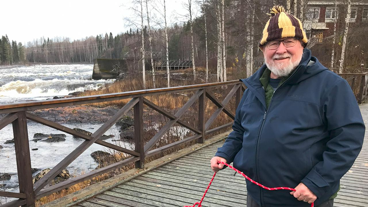en glad herre står på en bro över en fors med ett rep i handen.
