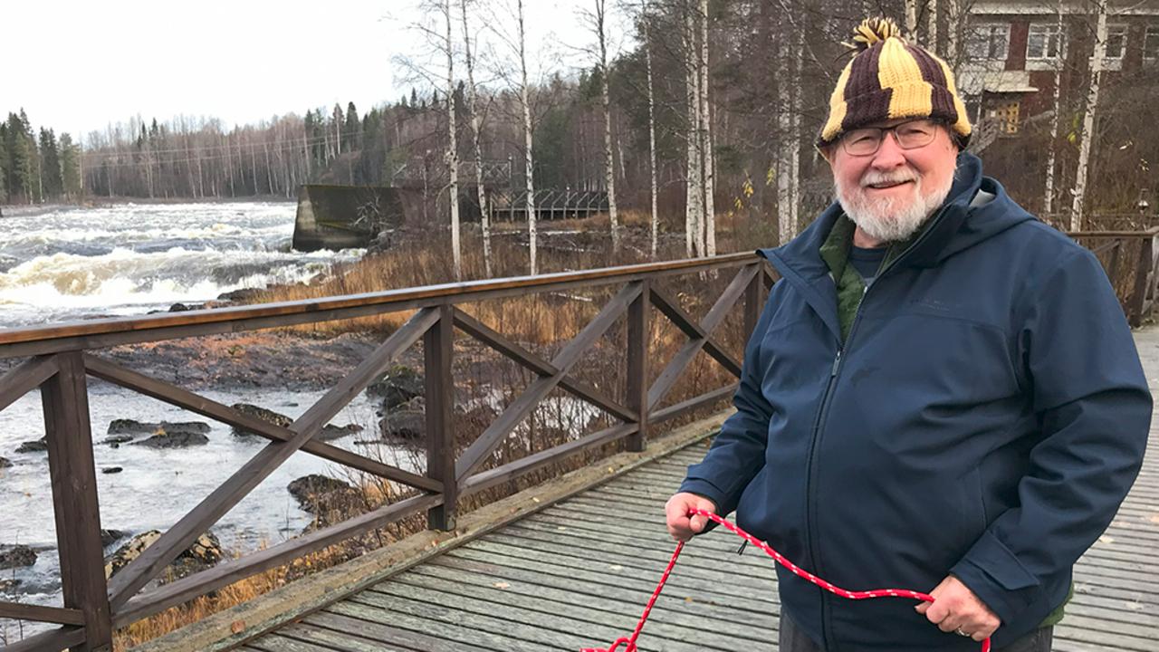 en glad herre står på en bro över en fors med ett rep i handen.