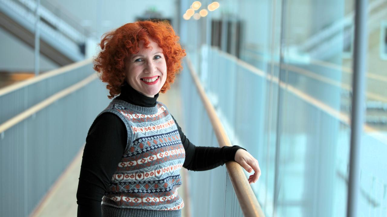 En kvinna med rött hår står på en balkong.