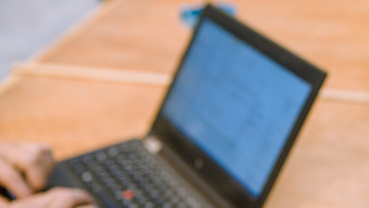 Närbild på person som håller i smartphone och en annan person som knappar på en bärbar dator.