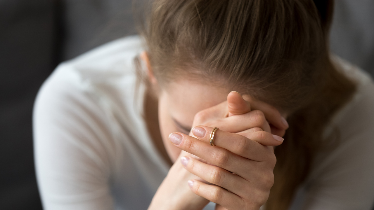 Kvinna som inte mår bra sitter lutad framåt med händerna knäppta framför ansiktet.