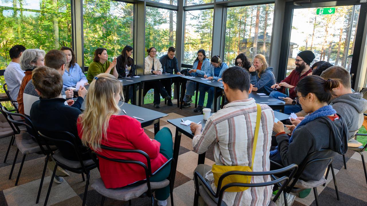 A group of people sitting in a circle at tables in a glass room.