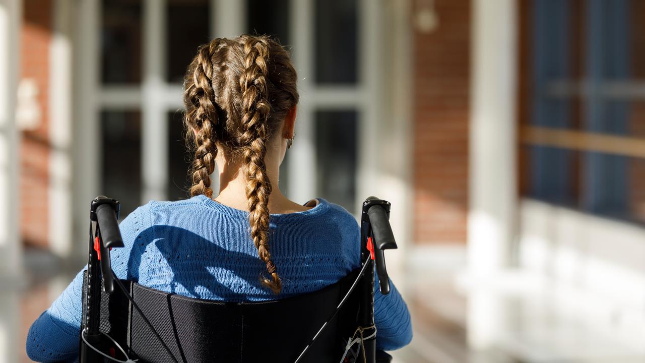 Flicka med flätor sitter i rullstol framför byggnad.