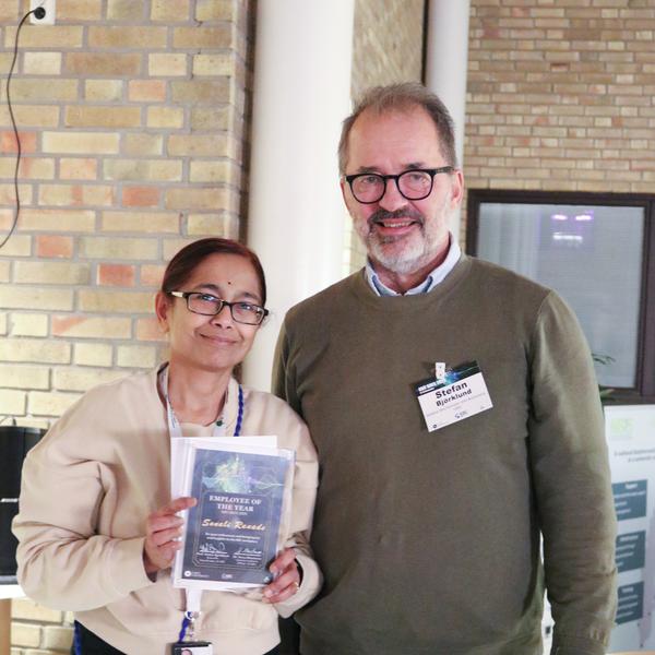 A woman holding an award and a man standing at the conference venue