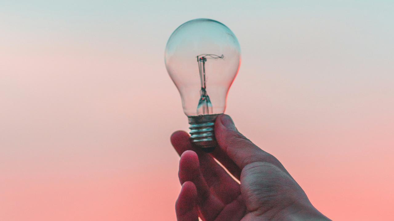 En hand som håller upp en glödlampa mot en rosa och blå bakgrund