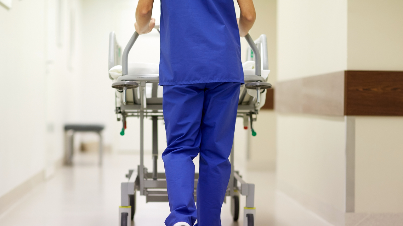 Vårdpersonal skjuter en säng på hjul med patient i en sjukhuskorridor.