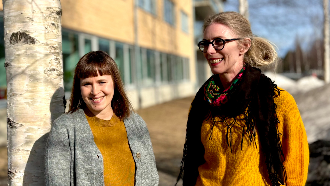 Två kvinnor står bredvid varandra nära ett träd