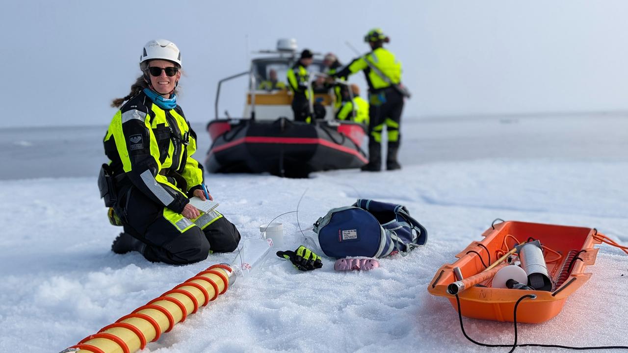 En kvinna arbetar med provtagning på is med en svävare i bakgrunden.