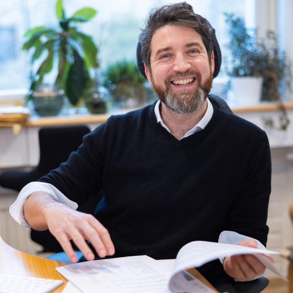 Bild på Olivier Keech sittande vid ett bord med dokument uppslagna framför sig.