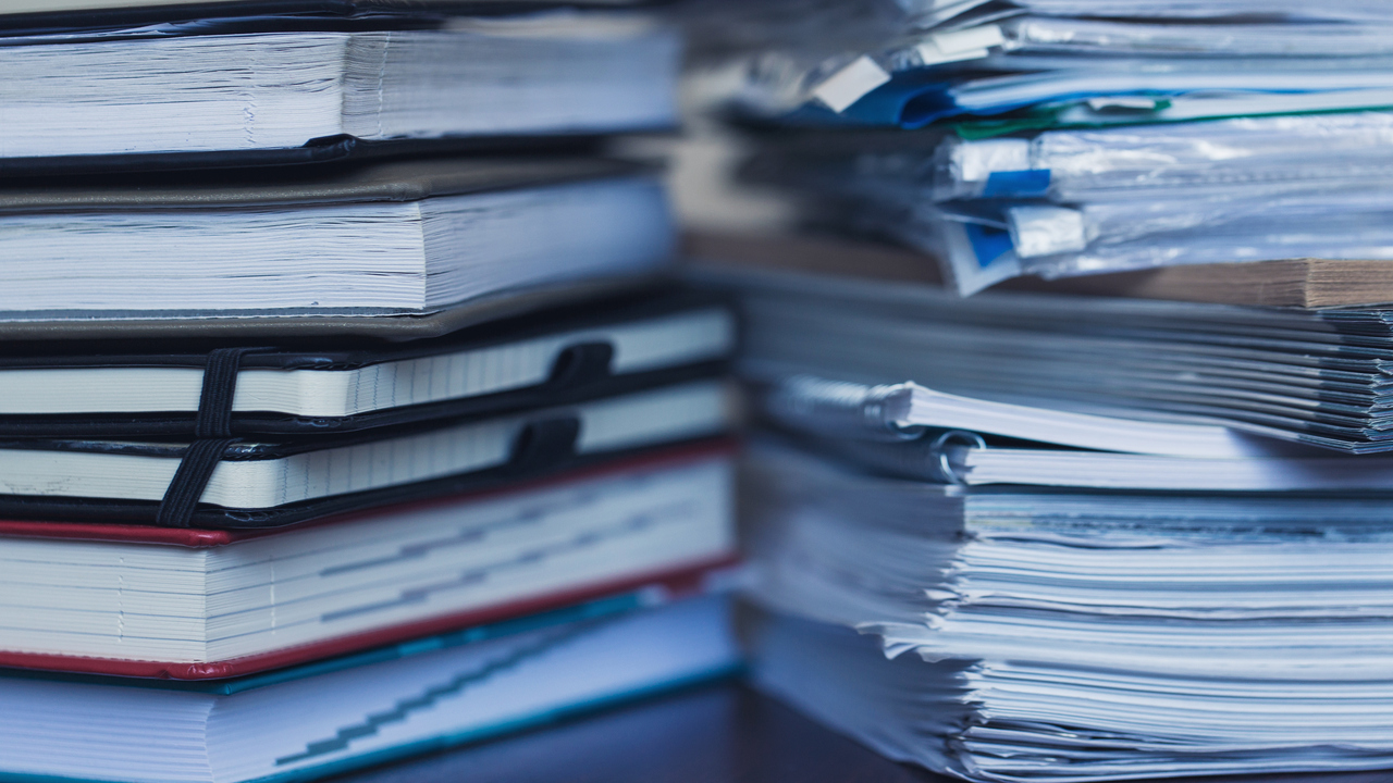 Närbild på två högar med böcker och tidskrifter på ett bord.